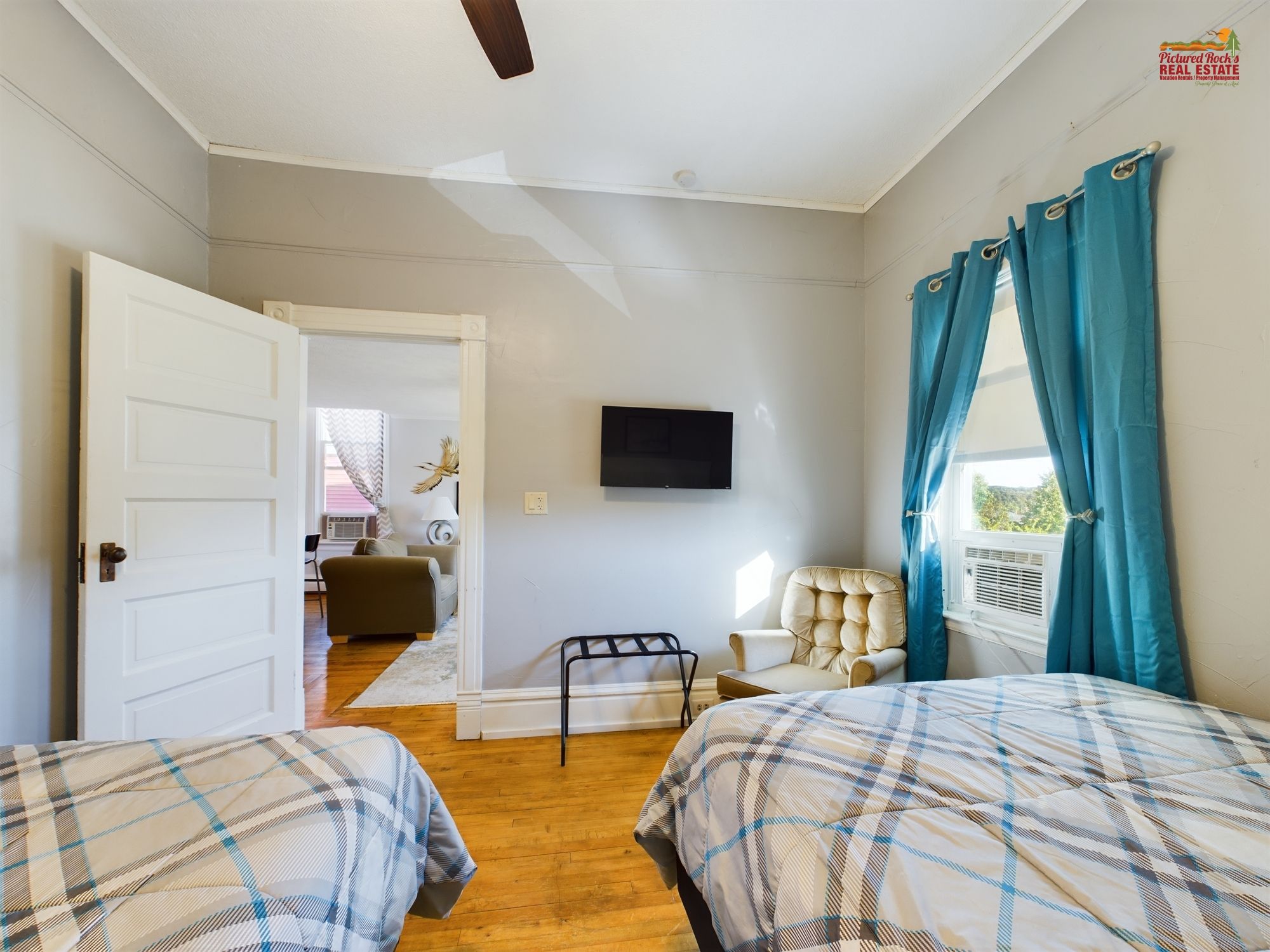 Una habitación con dos camas, televisión, una silla y ventana con cortinas.
