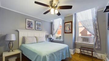 A bedroom with a bed, a ceiling fan, a window with curtains, and framed pictures on the wall.