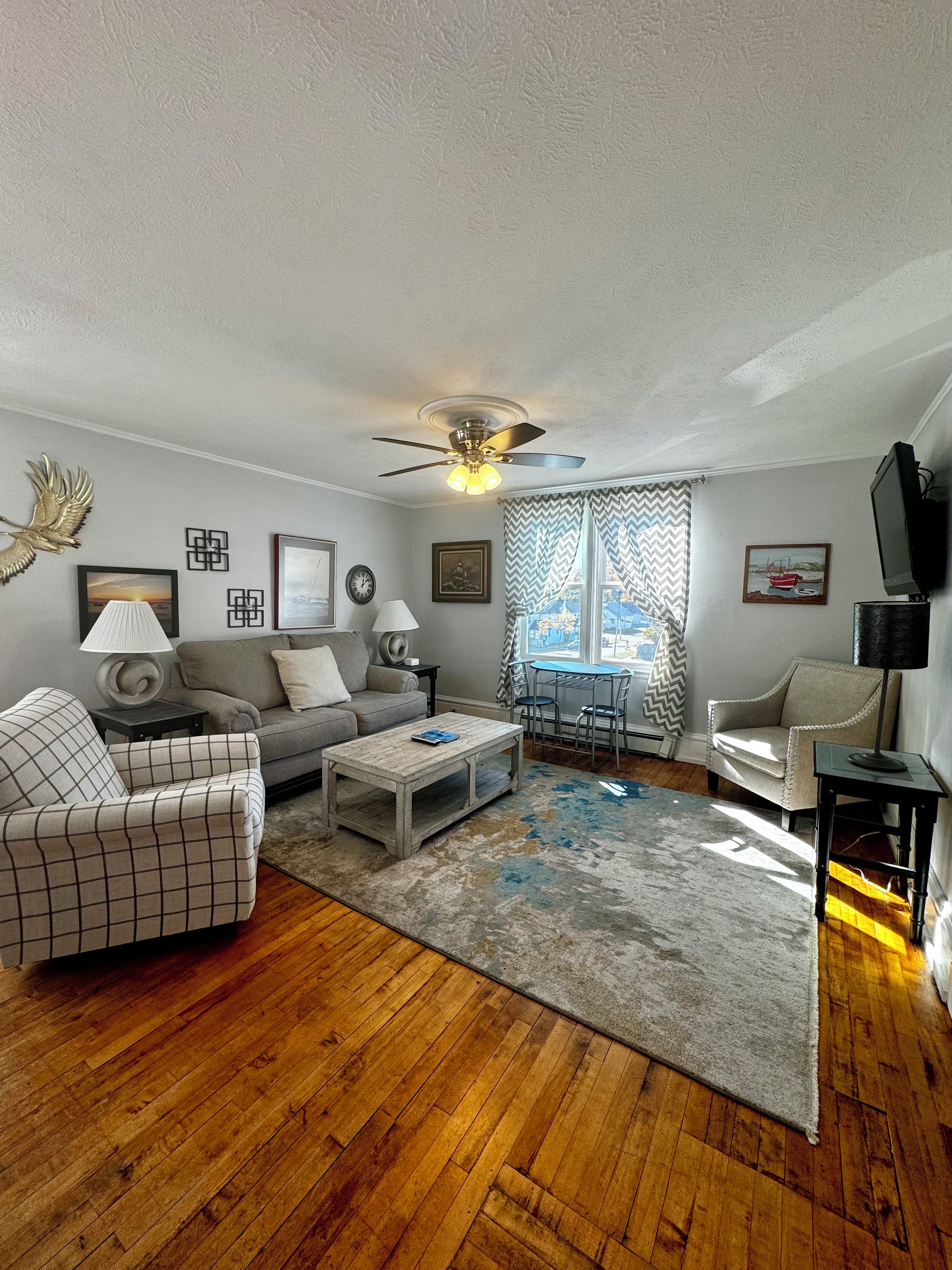 A living room with a wooden floor, a ceiling fan, a sofa, a coffee table, and a dining area with a table and chairs.