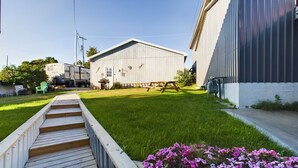A residential property with a wooden deck, a grassy yard, a small shed, and a trailer parked nearby. - SSVR2-Spacious, Downtown Munising Apartment (Munising)