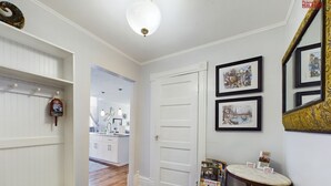 A hallway with a white door, a small table with magazines, and a mirror with a decorative frame. - SSVR2-Spacious, Downtown Munising Apartment (Munising)