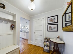 A hallway with a white door, a small table with magazines, and a mirror with a decorative frame. - SSVR2-Spacious, Downtown Munising Apartment (Munising)
