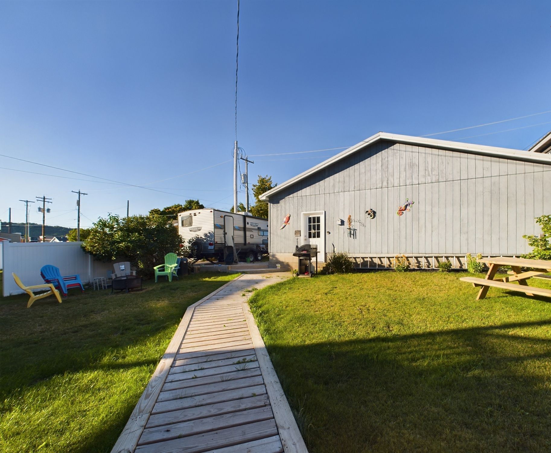 A backyard with a wooden deck leading to a building, a picnic table, and a camper parked nearby.