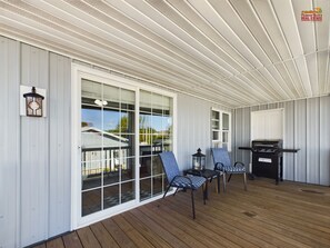 A covered porch with a grill, two chairs, and a lantern. - SSVR3-Cute 2nd Floor Apartment in Munising with a Balcony and Grill (Munising)