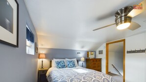 Un dormitorio con cama, mesita de noche, cómoda, ventilador de techo y una puerta.