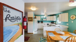 Una cocina con armarios blancos, una isla central y una zona de comedor con una mesa y sillas de madera.