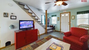 Una sala de estar con una escalera, un televisor, un sofá rojo, una mesa de centro y una estantería.
