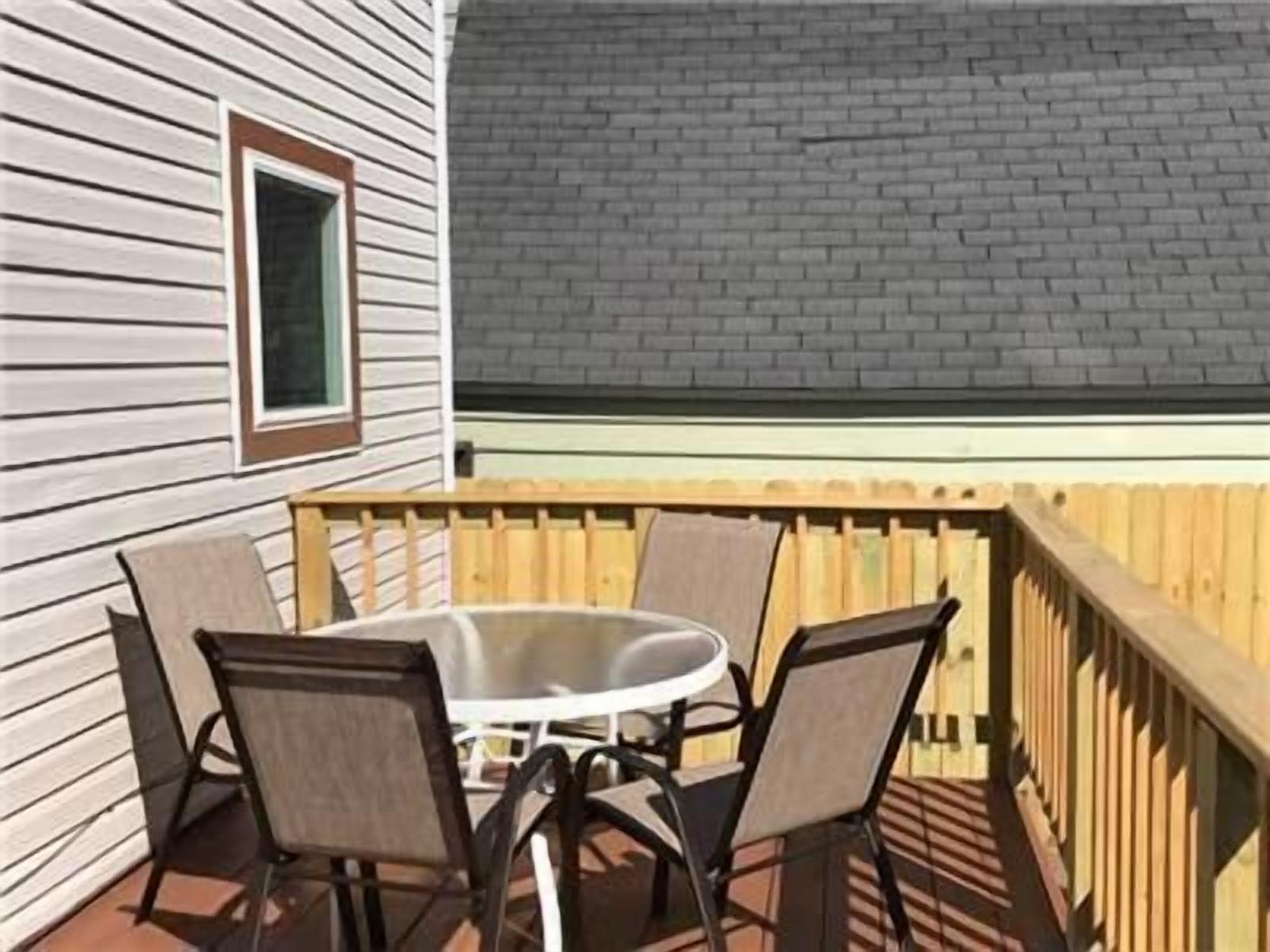 Une terrasse avec une table ronde et quatre chaises, une plateforme en bois et un mur en briques.