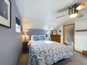 A bedroom with a bed, a nightstand, a dresser, a ceiling fan, and a door. - Rock House-Downtown Munising with Private Patio, Garage, Fire-pit & BBQ Grill (Munising)