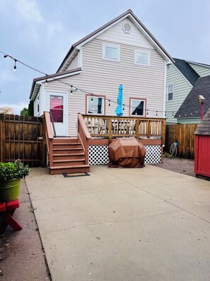 A house with a deck, a covered grill, and a wooden fence. - Rock House-Downtown Munising with Private Patio, Garage, Fire-pit & BBQ Grill (Munising)