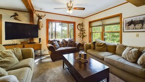 A cozy living room with a large flat-screen TV, a ceiling fan, and a fireplace.