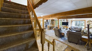 A wooden staircase leading to a living area with a fireplace, seating, and a television.