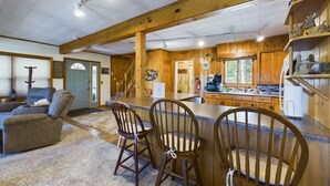 A rustic cabin interior with a dining area, wooden walls, and a kitchen.