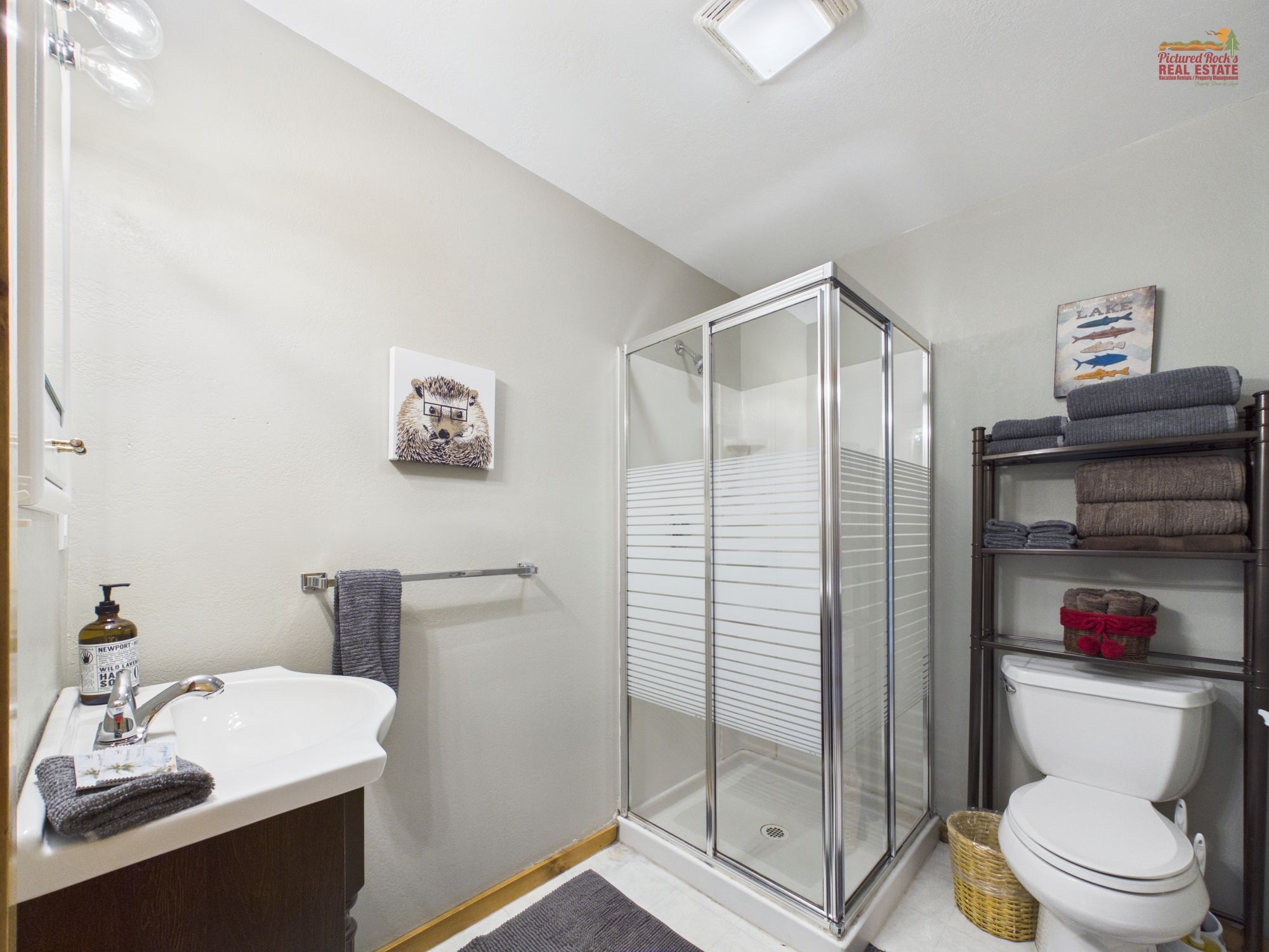A bathroom with a glass shower enclosure, a white sink, a toilet, and a shelf with towels.