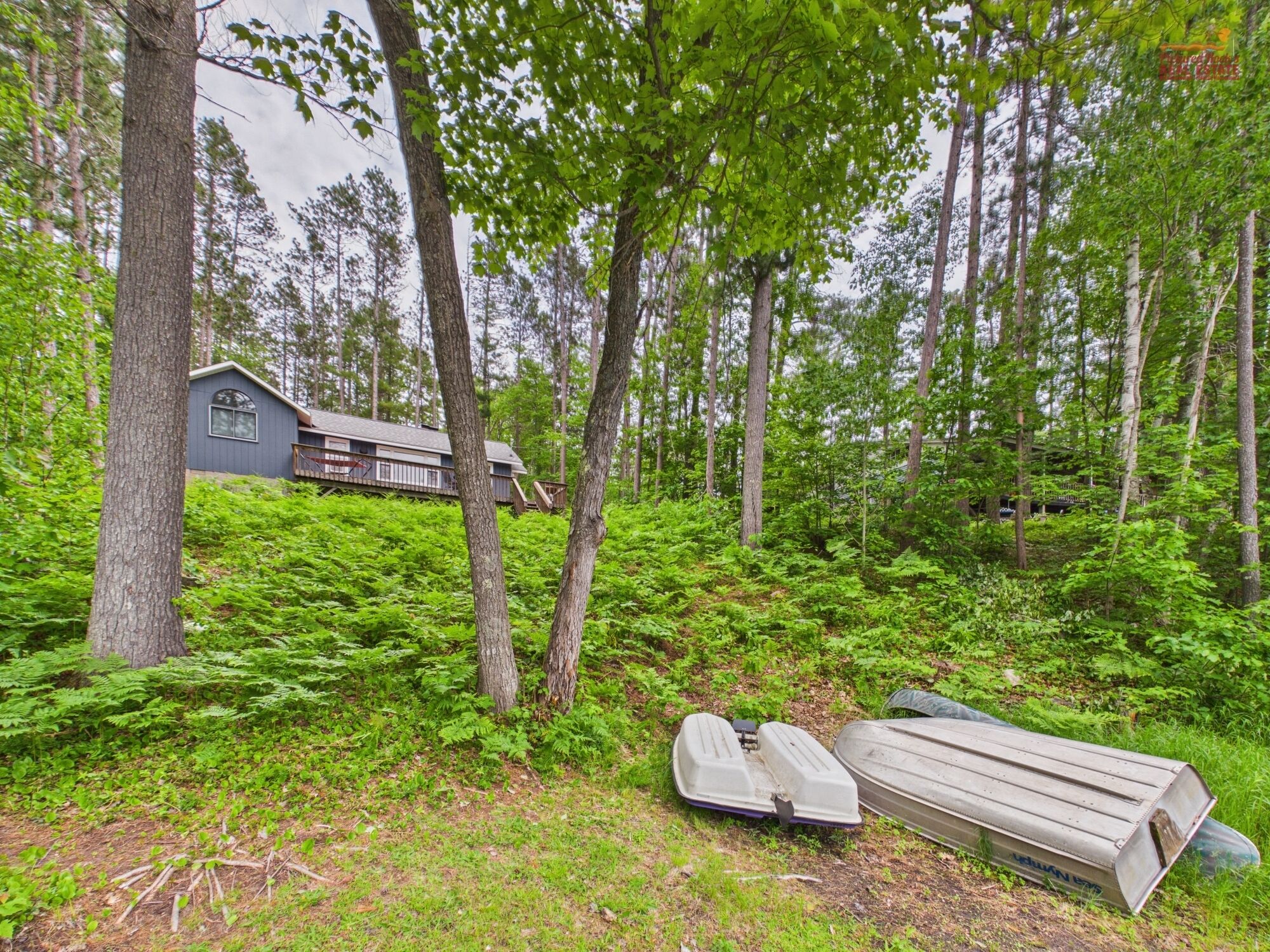 A cabin in a forest with a deck and a boat.