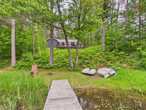 A wooden dock leading to a house surrounded by dense forest. - Cozy UP Cottage Near Pictured Rocks (Wetmore)