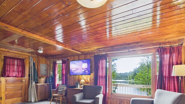 A wooden cabin interior with a television, a dining table, and a view of a lake.