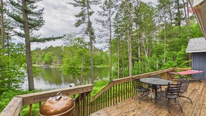 A wooden deck with a grill, outdoor table, and chairs overlooking a lake.