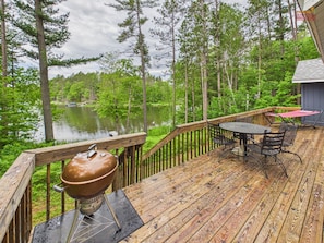 Une terrasse en bois avec un barbecue, une table et des chaises, le tout donnant sur un lac.