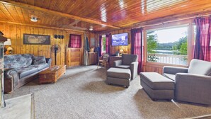 A wooden cabin interior with a sofa, armchairs, a television, and a fireplace.