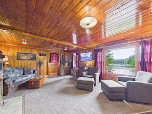 A wooden cabin interior with a sofa, armchairs, a television, and a fireplace.