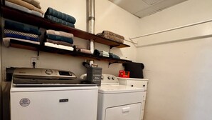 Une buanderie équipée d’un lave-linge et d’un sèche-linge à chargement frontal, avec des étagères en bois au-dessus pour ranger les serviettes pliées, et une bouche d’aération visible au plafond.