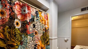 Une salle de bain avec un plancher en bois, un lavabo blanc et un rideau de douche à motifs floraux.