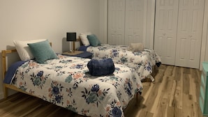 Une chambre à coucher avec deux lits, chacun agrémenté de draps à motifs floraux, une table de chevet avec une lampe et une armoire à deux portes.