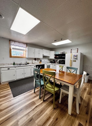 Cozinha compacta com armários brancos, uma mesa de jantar de madeira e uma janela com vista.