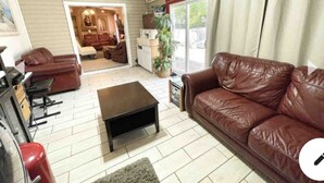 Una sala de estar con un sofá de cuero marrón, una mesa de centro de madera y un refrigerador antiguo rojo.