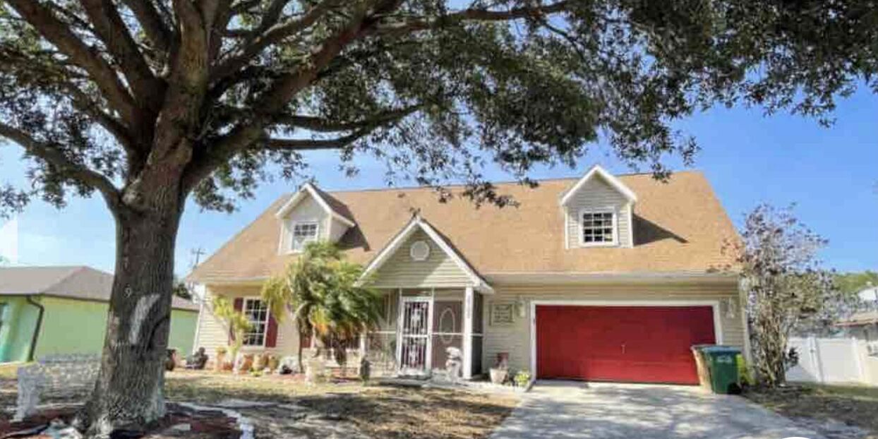 A two-story house with a red garage door, a front porch, and a large tree in front.