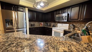 Una cocina con encimeras de granito, electrodomésticos de acero inoxidable, muebles oscuros y una lámpara colgante.