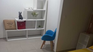 A bedroom with a yellow bed, a blue chair, a white shelf unit, and a small plant.