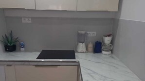 A kitchen with white cabinets, a black countertop, a blender, a coffee maker, and a potted plant.