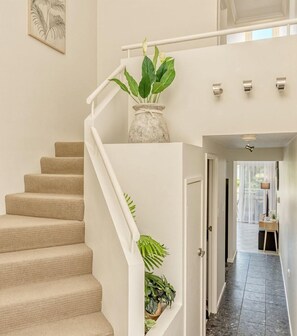 Stairs lead to a hallway with a view of an outdoor area featuring a table and chairs.