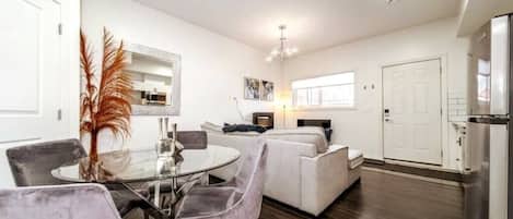 A modern living room with a dining area, a sofa, and a kitchen area with a refrigerator.