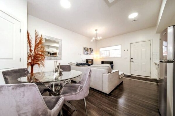 A modern living room with a dining area, a sofa, and a kitchen area with a refrigerator.