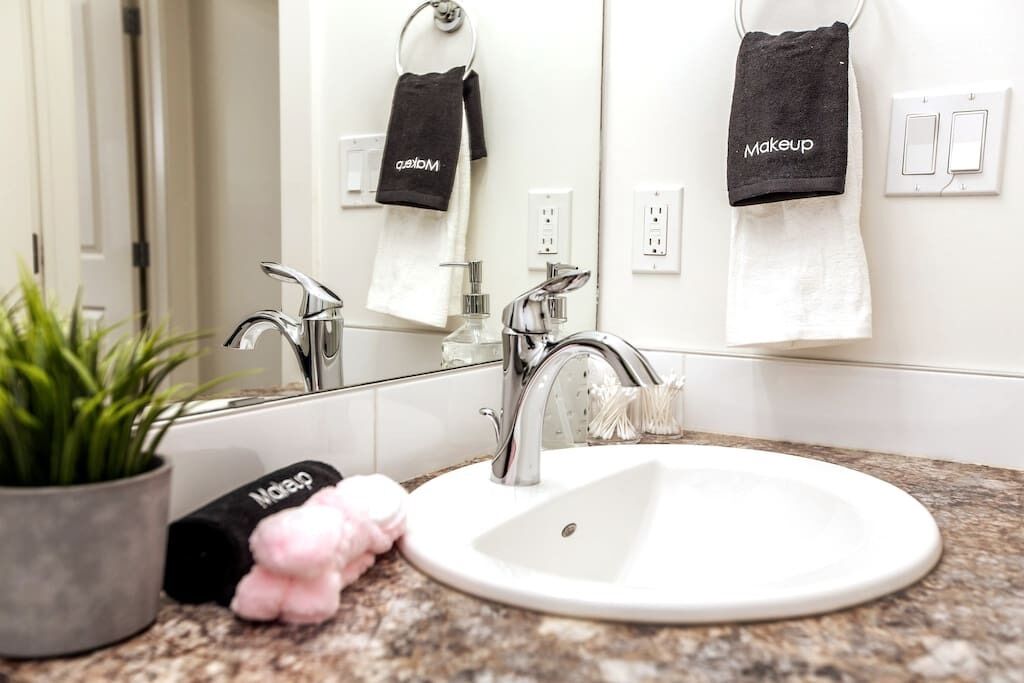 A bathroom with a white sink, two faucets, a mirror, and towels hanging on a rack.