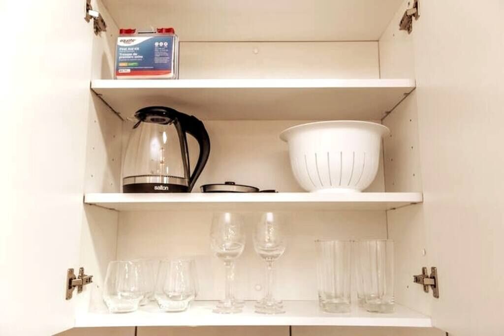 A white shelf with a box, a kettle, a colander, and several glasses.