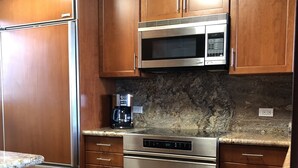 A kitchen with wooden cabinets, a stainless steel refrigerator, a microwave, a coffee maker, and an oven.