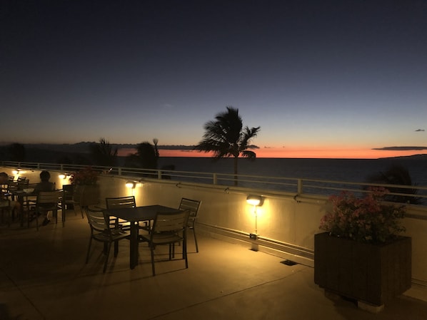 A terrace with tables and chairs, overlooking a sunset over the sea.
