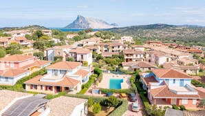 A coastal residential area with terraced houses, a swimming pool, and a prominent mountain in the background. - All have their own entrance and are located in four-family villas.Elegantly furnished, they have a small garden with furnished covered veranda or furnished covered terrace.Composed of living room with kitchenette and sofa, bedroom with double bed, room w (Monte Petrosu)
