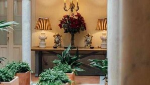 A corridor with a central floral arrangement, flanked by potted plants and a candelabra.