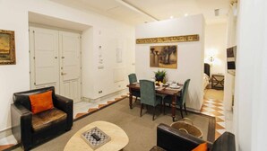 A hotel room with a dining area, a sofa, a coffee table, and a painting on the wall.