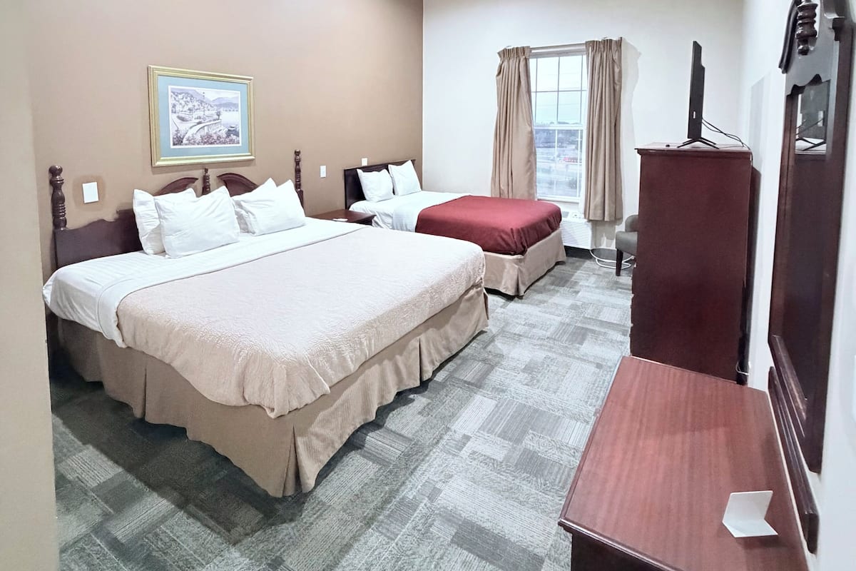 A hotel room with two beds, a desk, a television, and a window with curtains.