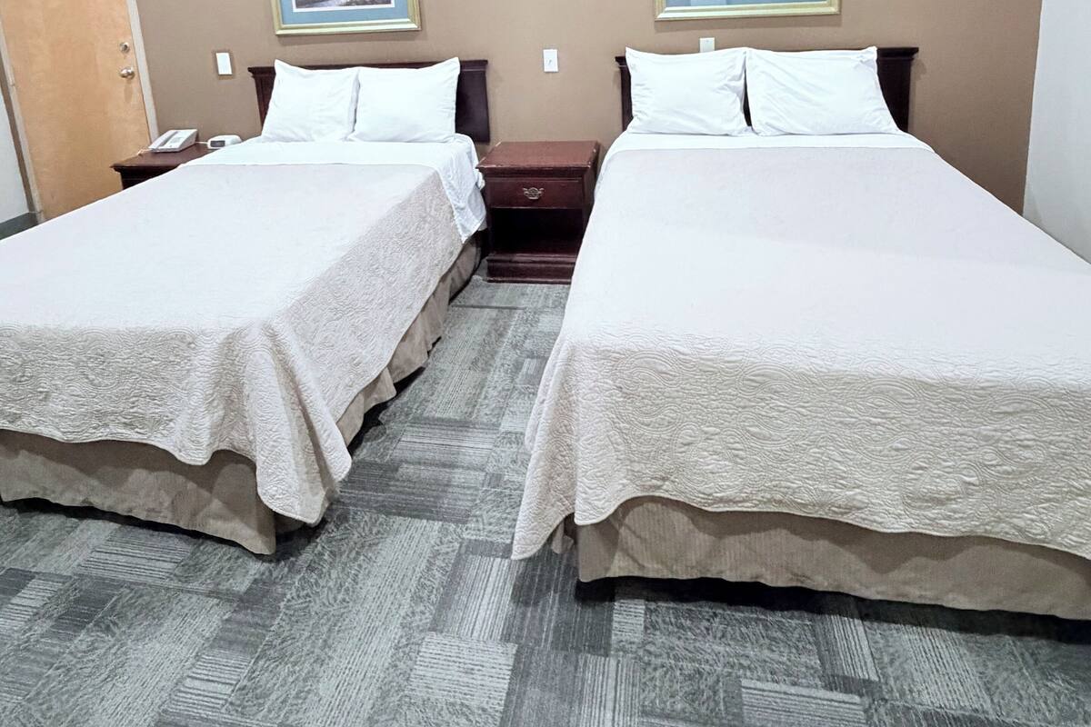 A hotel room with two beds, a door, a nightstand, and two framed pictures on the wall.