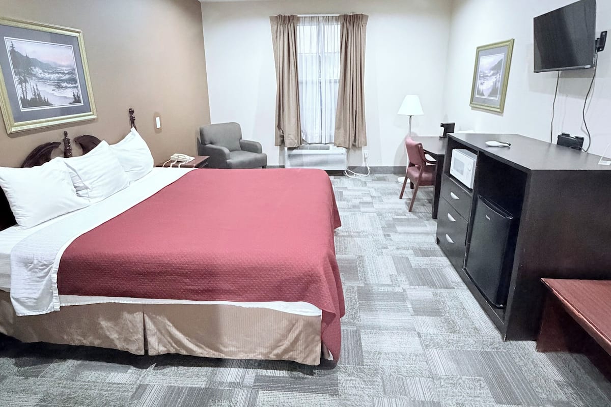 A hotel room with a bed, desk, chair, television, and artwork on the walls.