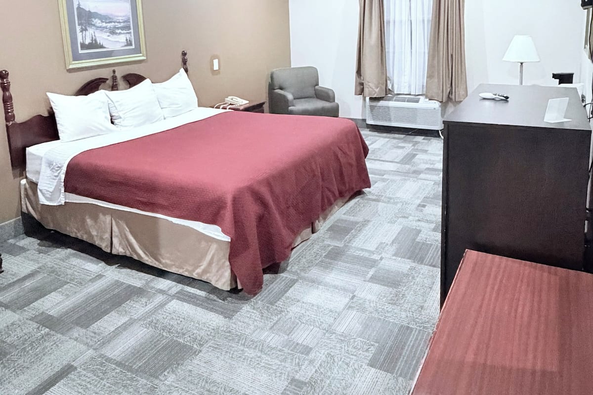 A hotel room with a bed, a desk, a chair, a television, and a picture on the wall.