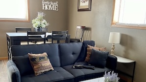 A living room with a sectional sofa, a coffee table, a dining table with chairs, a lamp, and a wall sign. - Store that boat inside!  Blocks to boat ramps/Marina & Restaurant (Chamberlain)