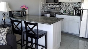 A modern kitchen with white cabinets, a microwave, a stove, and a refrigerator. There is a dining area with a table and chairs.